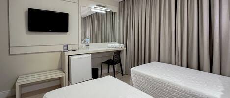 A hotel room with a bed, a desk with a computer, a television, and a large window with curtains.