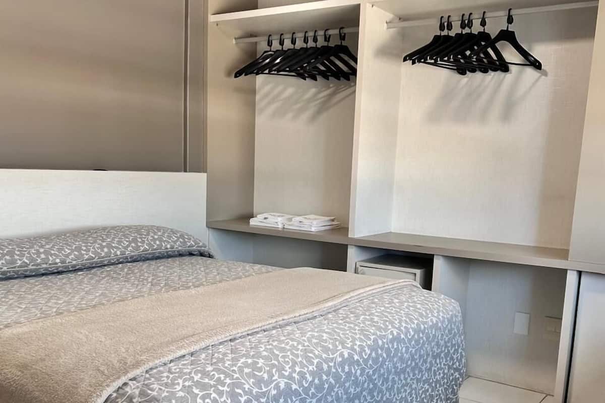 Une chambre à coucher avec un lit, une armoire et une étagère où sont suspendus des vêtements.