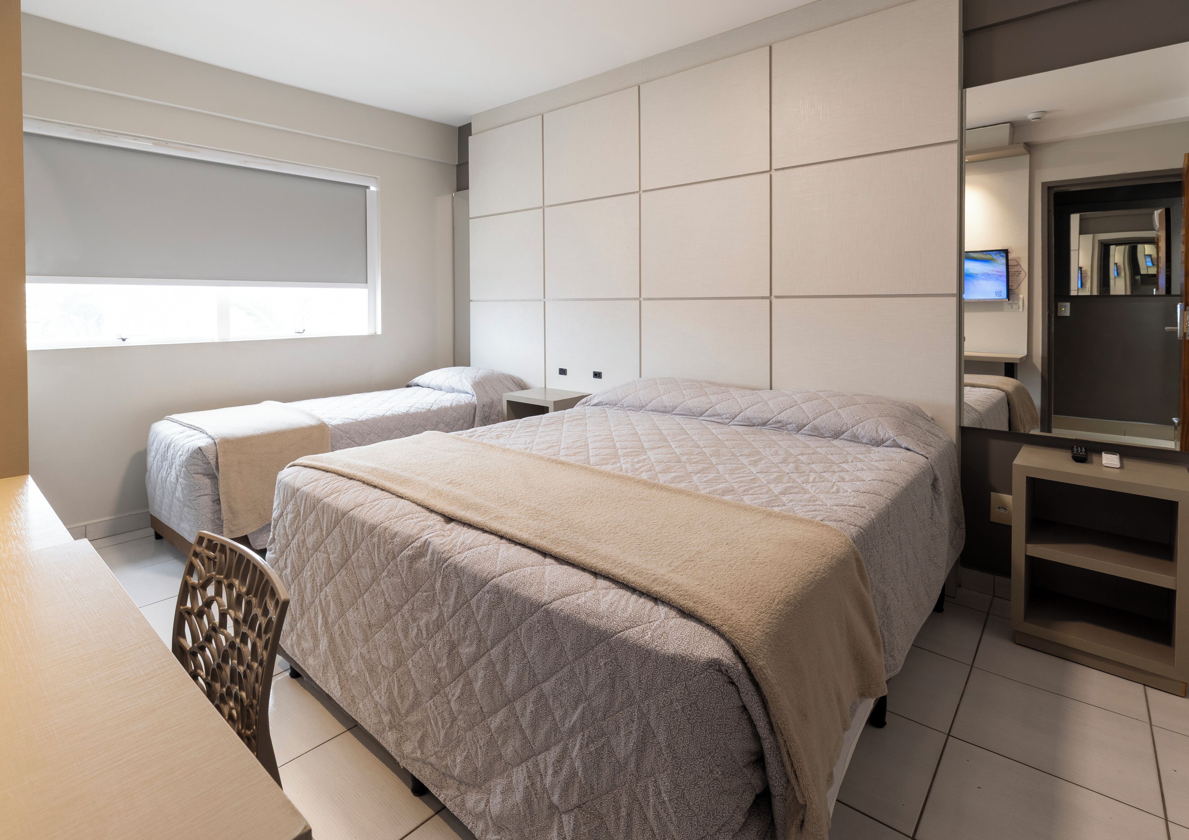 Une chambre d’hôtel avec deux lits, un bureau, une chaise, un miroir et un téléviseur.