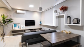A modern living room with a sofa, a TV, a coffee maker, and a shelf with decorative items. - Hotel Palmas Executivo (Balneário Camboriú)