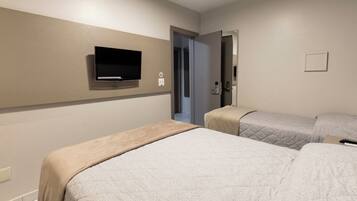 Ein Hotelzimmer mit zwei Betten, einem an der Wand befestigten Fernseher und einer Tür zu einem weiteren Raum.