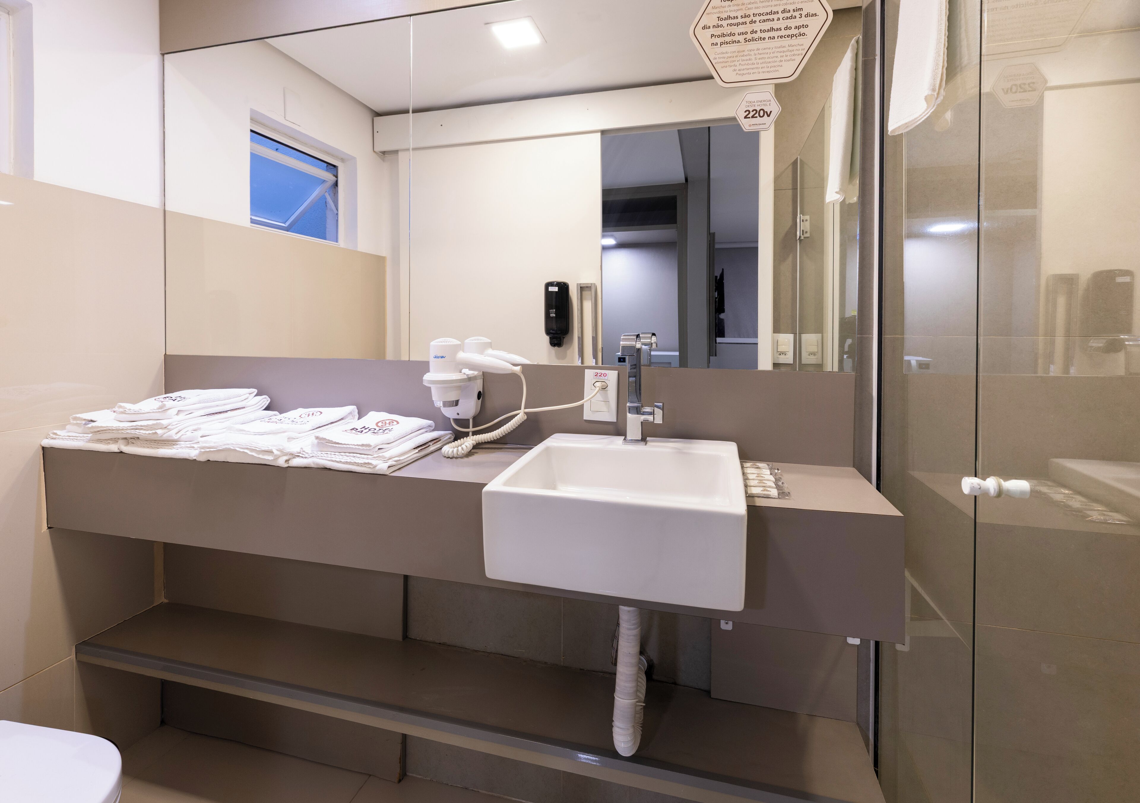 A modern bathroom with a white sink, a mirror, and a towel dispenser.