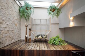 A wooden deck with a woven chair, a wooden sculpture, and hanging plants. - Hotel Palmas Executivo (Balneário Camboriú)