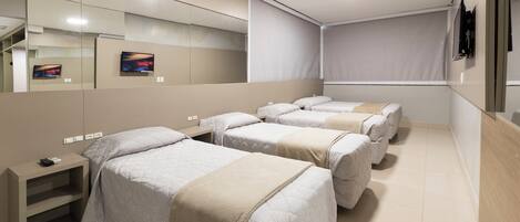 A hotel room with four beds, a TV, a desk, and a mirror.