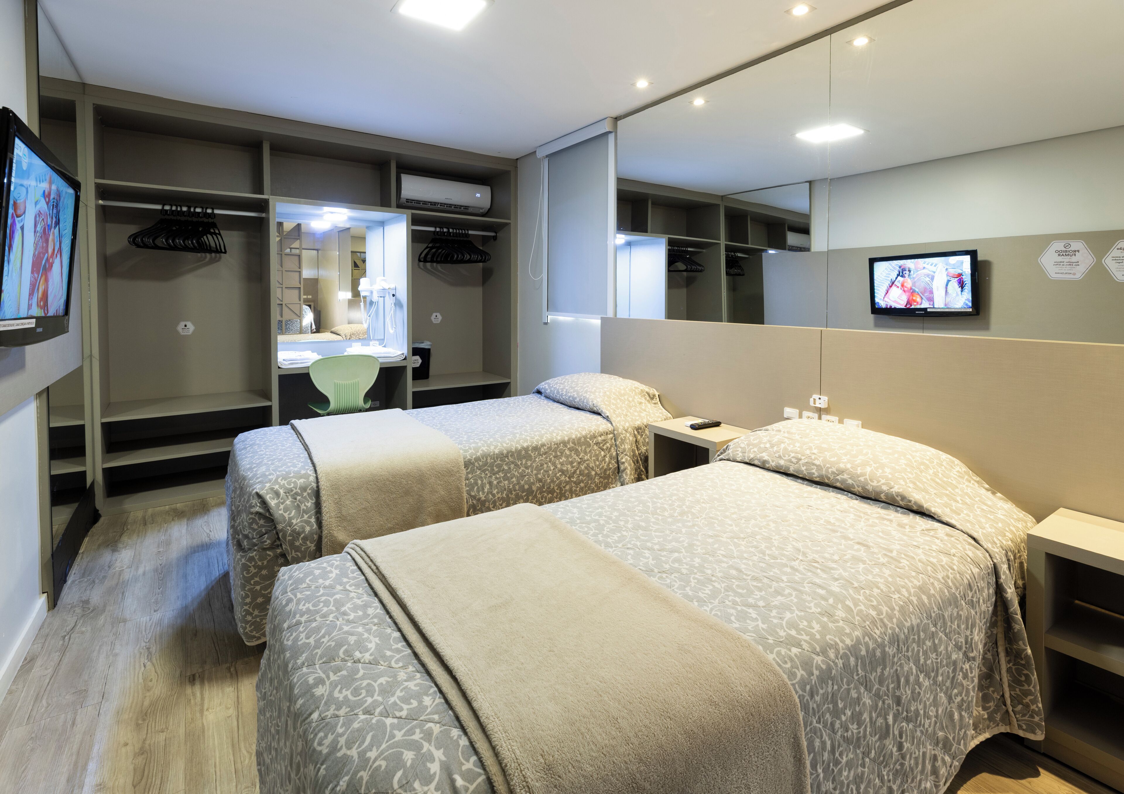 Habitación de hotel con dos camas, un escritorio, una silla, un televisor y un armario.