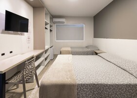 Un dormitorio con una cama, un escritorio, una silla, un televisor y un aire acondicionado.