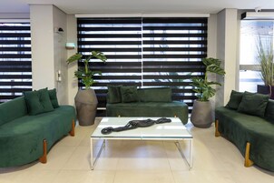 Una sala de estar moderna con un juego de sofá verde, una mesa de centro de vidrio y ventanas amplias con persianas horizontales.