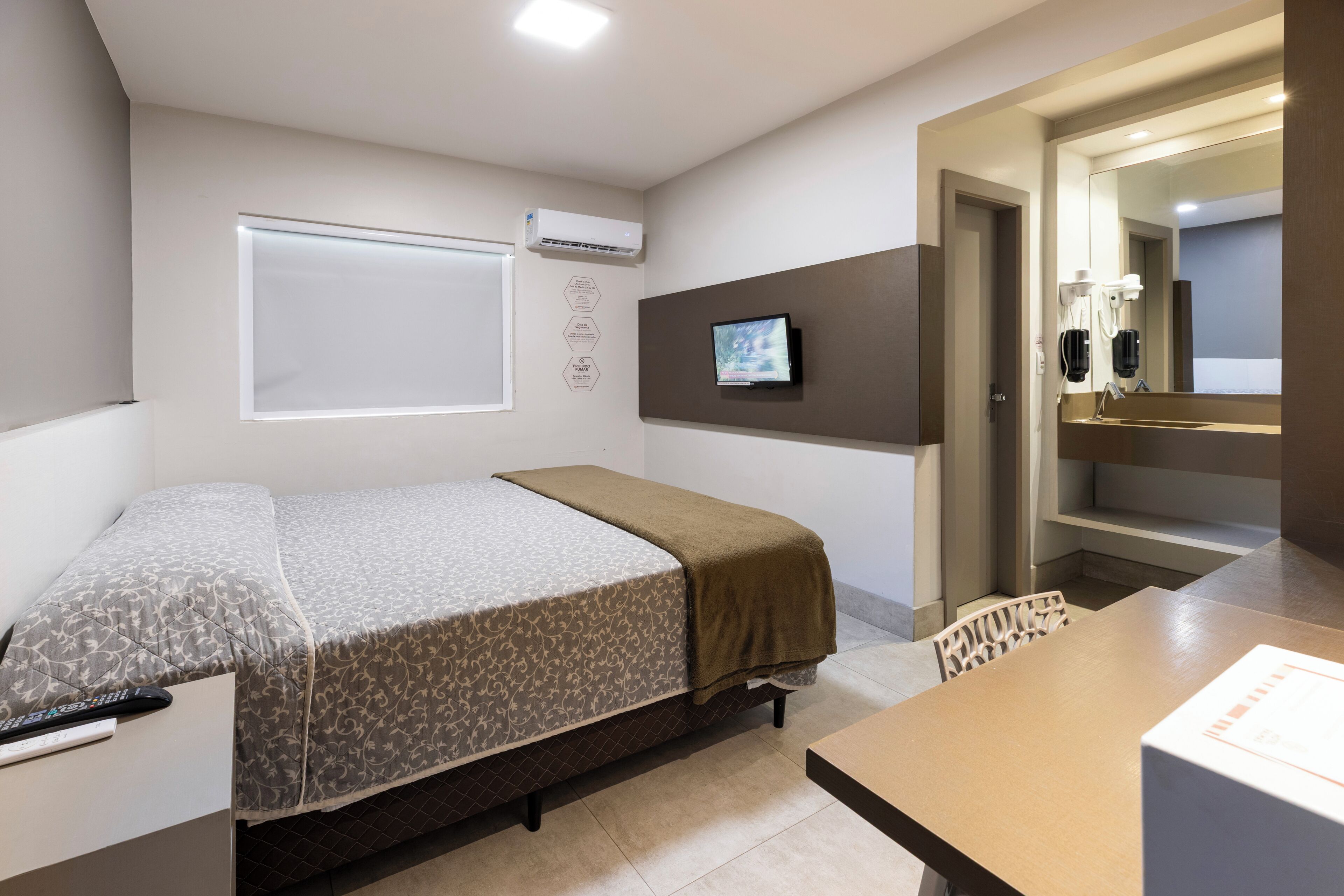 A hotel room with a bed, a desk, a television, and a bathroom visible through an open door.