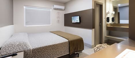 Habitación de hotel con cama, escritorio, televisión y baño visible a través de una puerta abierta.