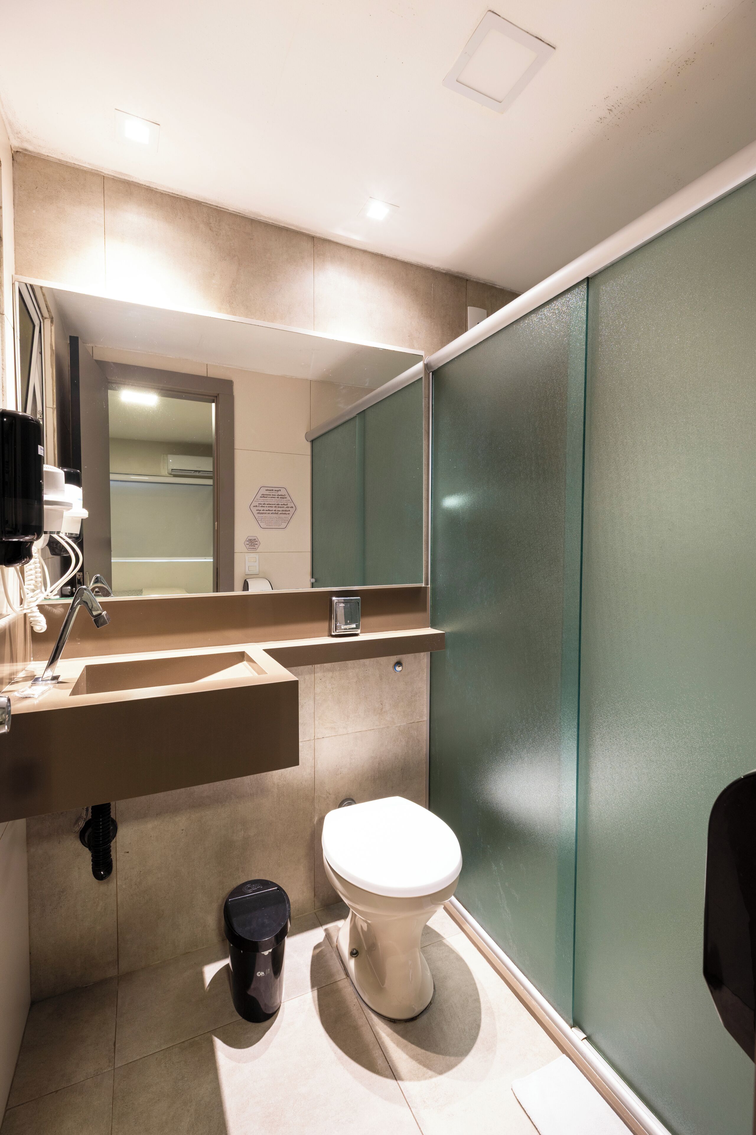 A modern bathroom with a sink, mirror, toilet, and a trash bin.