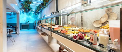 A buffet area with a variety of food items, including fruits, pastries, and a milk dispenser.
