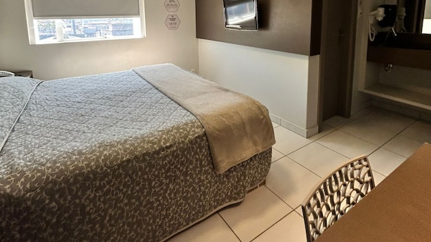 A hotel room with a bed, a TV mounted on the wall, an air conditioning unit, and a window with blinds. - Hotel Palmas Executivo (Balneário Camboriú)
