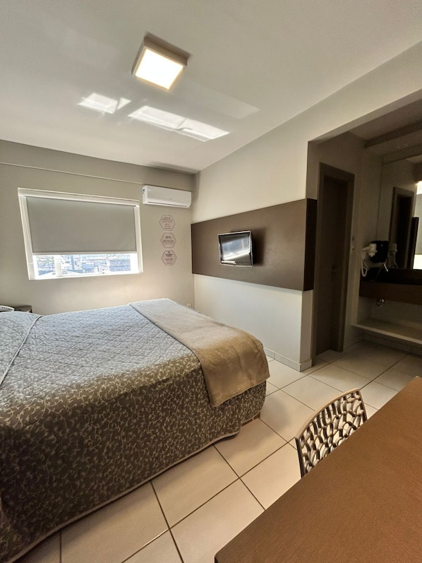 Une chambre d’hôtel équipée d’un lit, d’un téléviseur fixé au mur, d’un appareil de climatisation et d’une fenêtre avec des stores.
