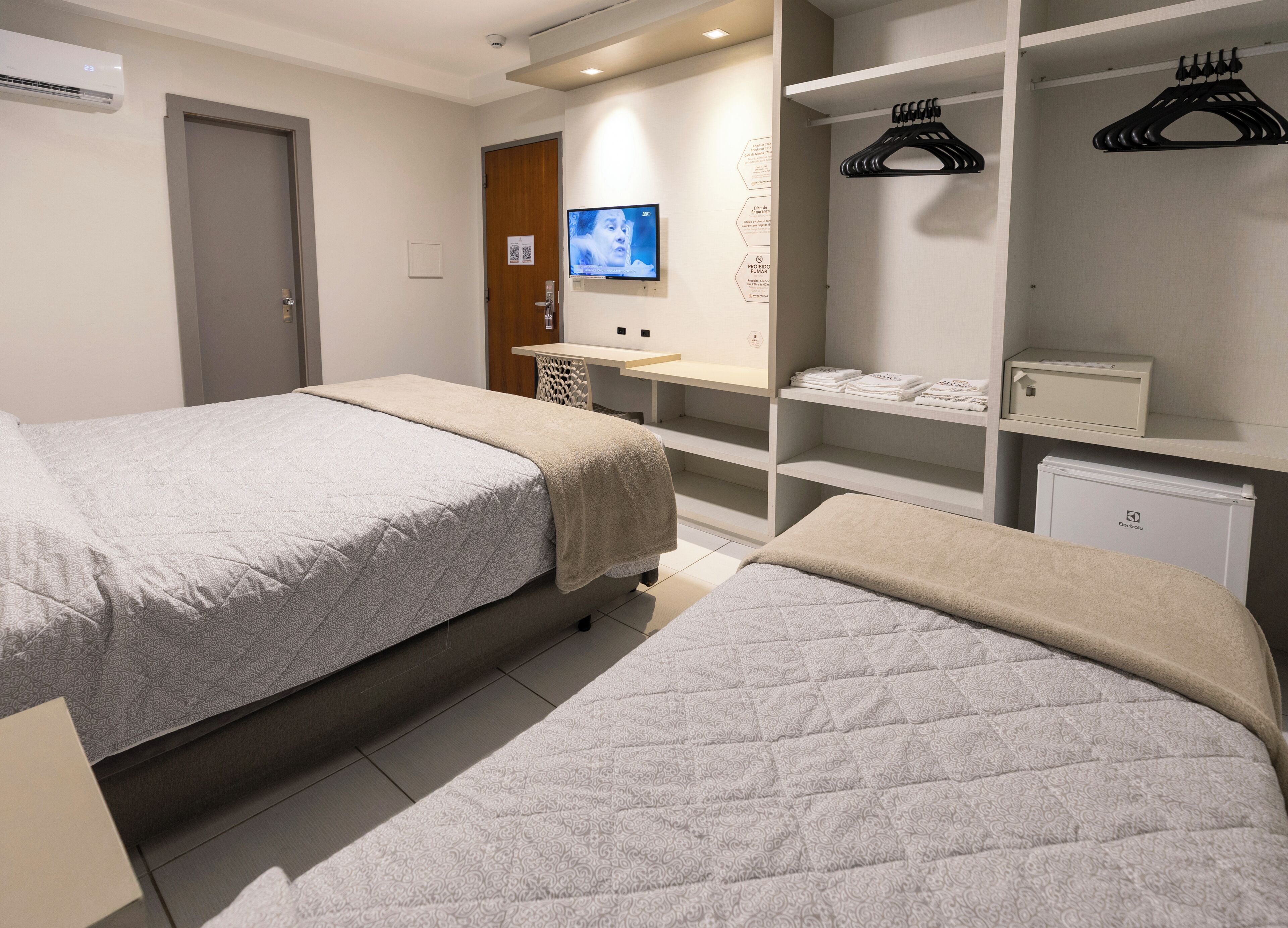 Habitación de hotel con dos camas, televisor, minibar y armario con perchas.
