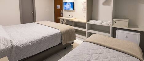 A hotel room with two beds, a TV, a minibar, and a wardrobe with hangers.