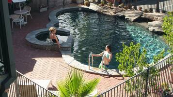 Guests can enjoy a refreshing swim in the pool surrounded by lush greenery and a brick patio.