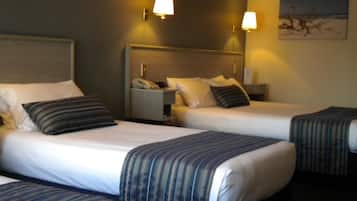 Een hotelkamer met twee eenpersoonsbedden, elk voorzien van een gestreept dekbedovertrek, een nachtkastje met een lamp en een schilderij aan de muur.