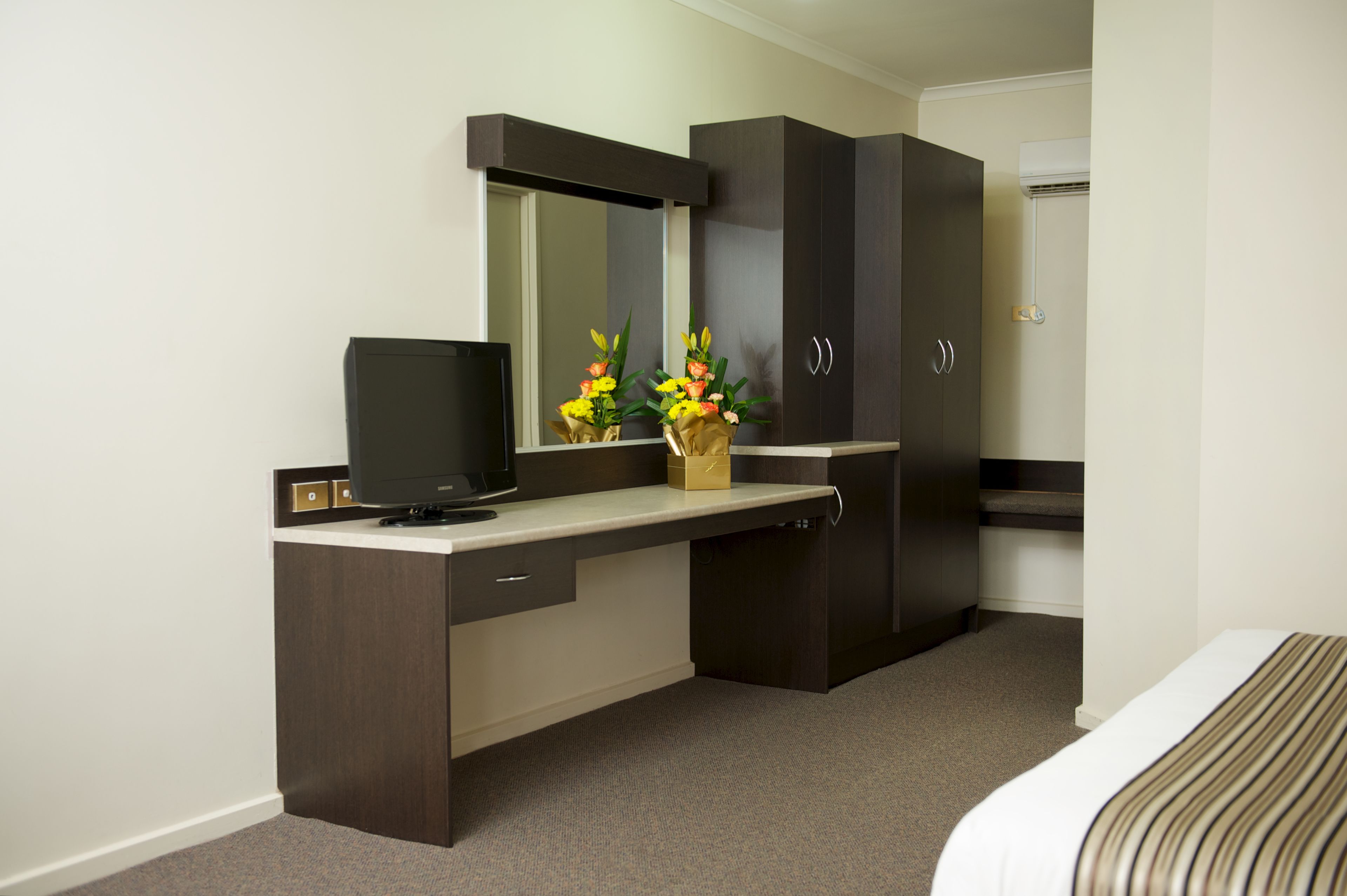 Hotelkamer met een donker houten bureau, een flatscreen televisie, een spiegel, een kledingkast en een bed met een gestreept dekbed.