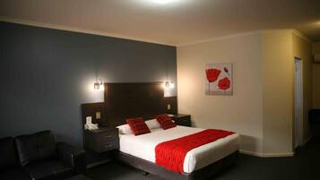 A hotel room with a large bed, two bedside tables, a nightstand, a black leather sofa, and a red flower painting on the wall.