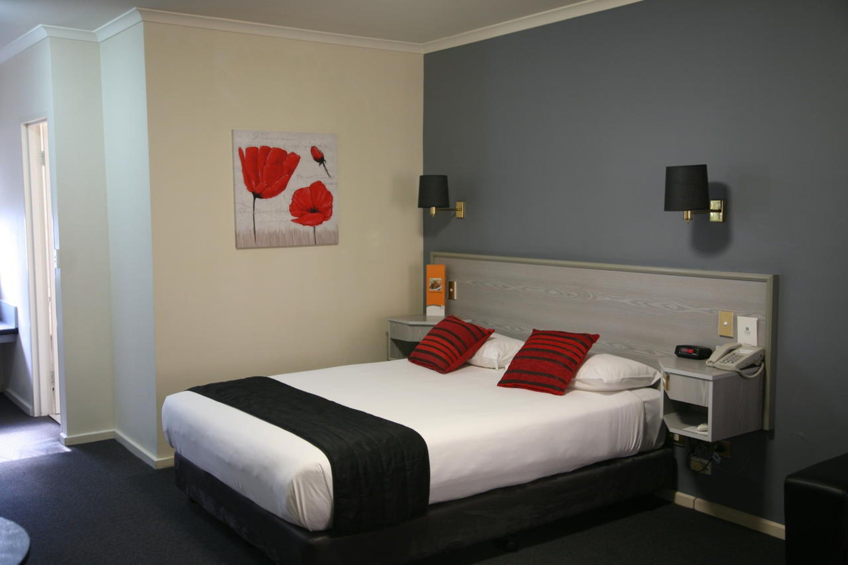 Habitación de hotel con cama, dos mesitas de noche, un teléfono y una lámpara de pared.