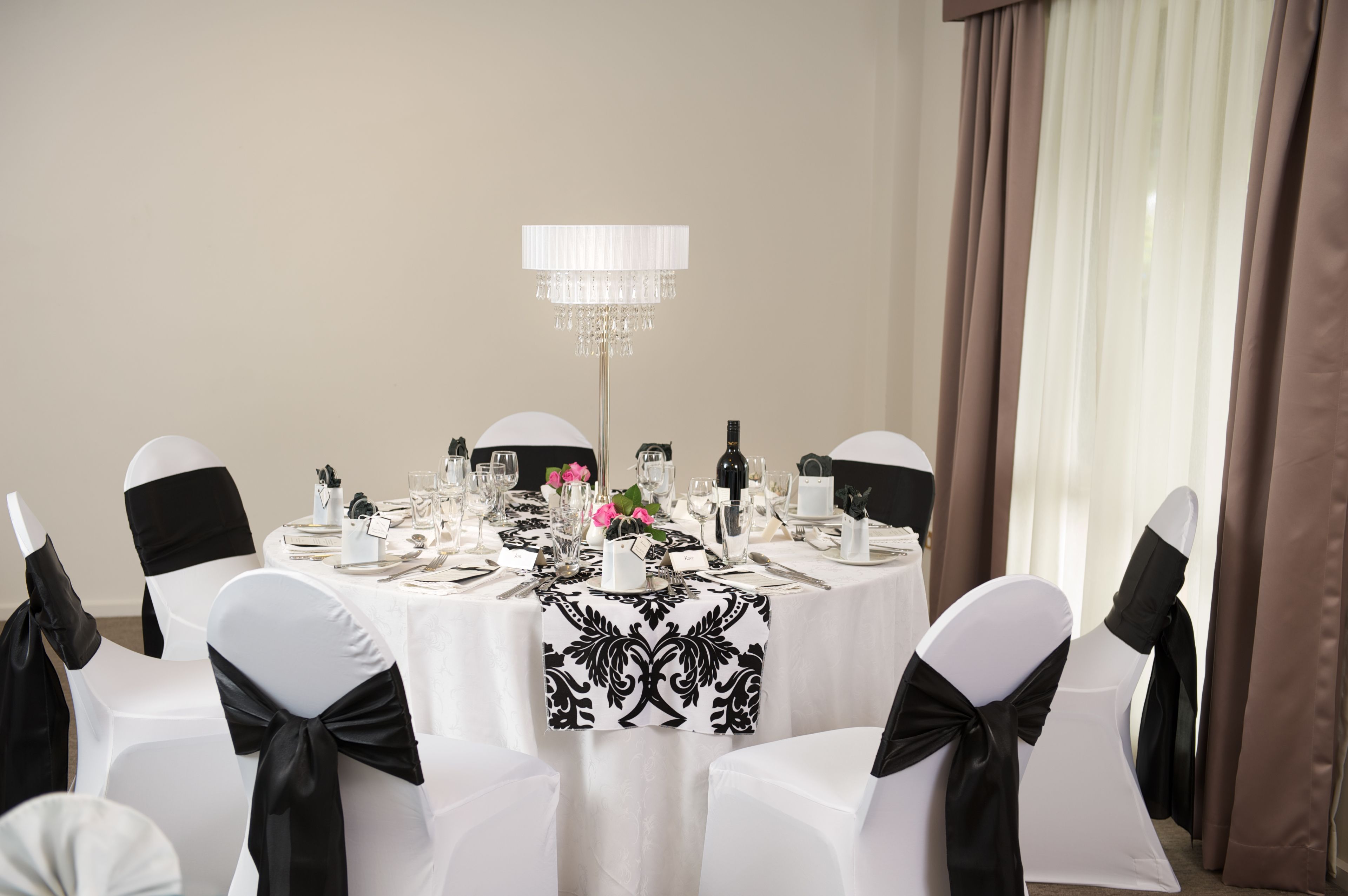 A banquet hall with round tables set for a formal event, featuring white tablecloths, black sashes, and a chandelier.