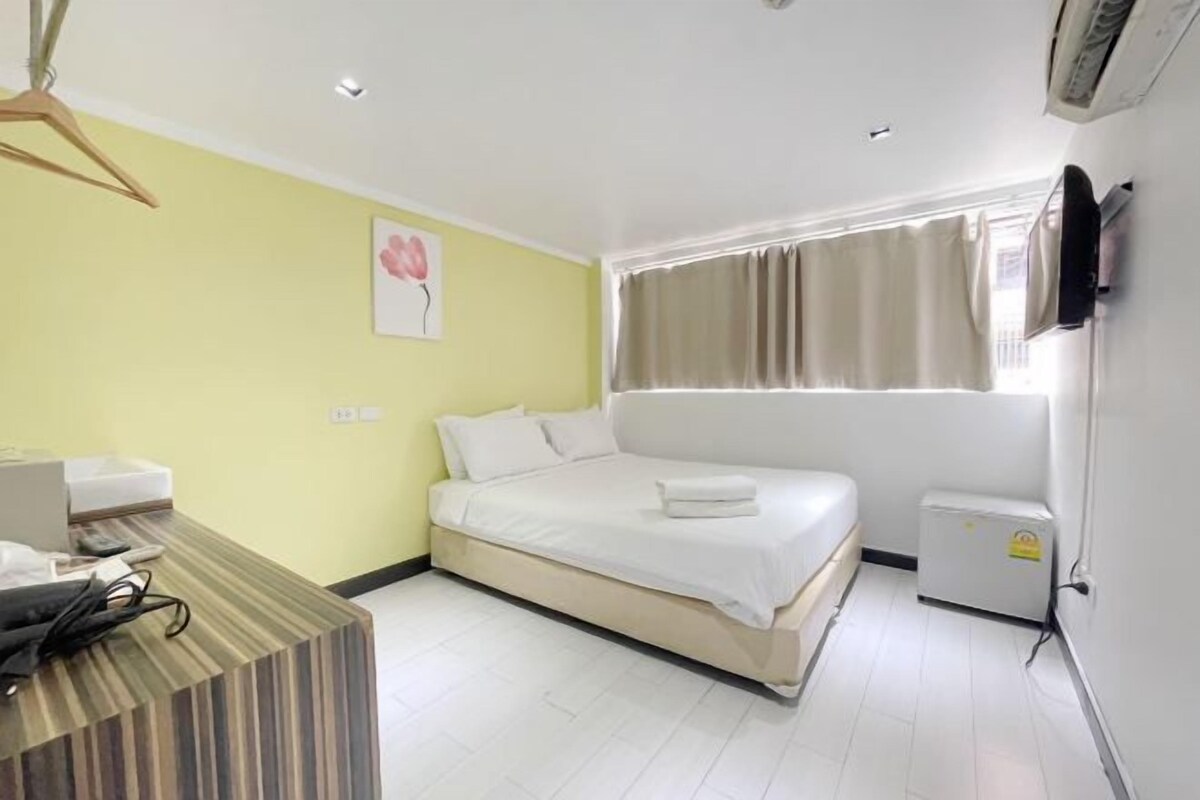 A hotel room with a bed, a bedside table, a small heater, and a window with curtains.