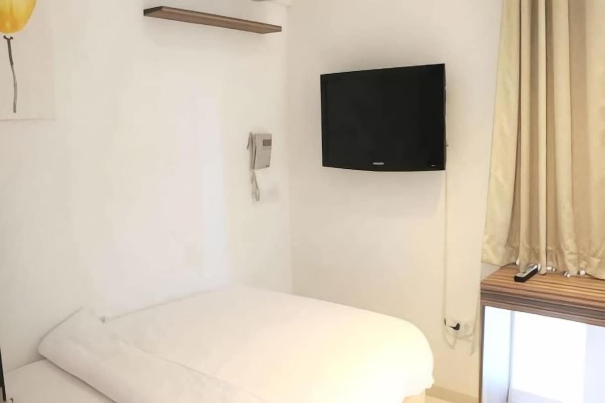 Ein Zimmer mit einem Bett, einem Wand-Fernseher, einem Telefon und einem Fenster mit Vorhängen.