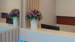 A reception area with a counter, two flower arrangements, and a mirror reflecting the space. - Nantra Ploenchit (Bangkok)