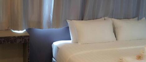 A hotel room with a bed, curtains, a nightstand, and a wooden floor.