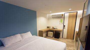 A hotel room with a bed, a desk, a small refrigerator, and a mirror.