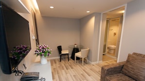 A modern living room with a flat-screen TV, a small table with a vase of flowers, a sofa, and a chair. - Nantra Ploenchit (Bangkok)