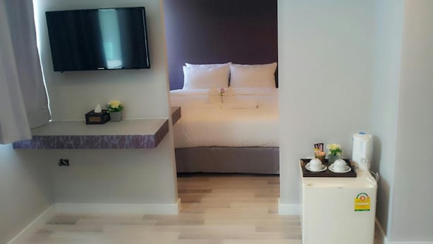 A hotel room with a bed, a TV mounted on the wall, a small table with a plant, and a refrigerator. - Nantra Ploenchit (Bangkok)