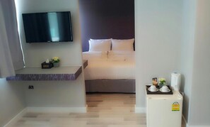 A hotel room with a bed, a TV mounted on the wall, a small table with a plant, and a refrigerator. - Nantra Ploenchit (Bangkok)