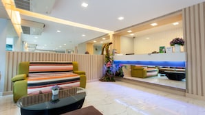 A modern lobby with a striped sofa, a glass coffee table, and a reception desk with a plant. - Nantra Ploenchit (Bangkok)
