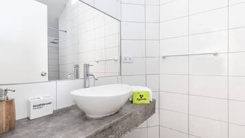 Un baño moderno con lavamanos blanco, espejo y paredes con azulejos.