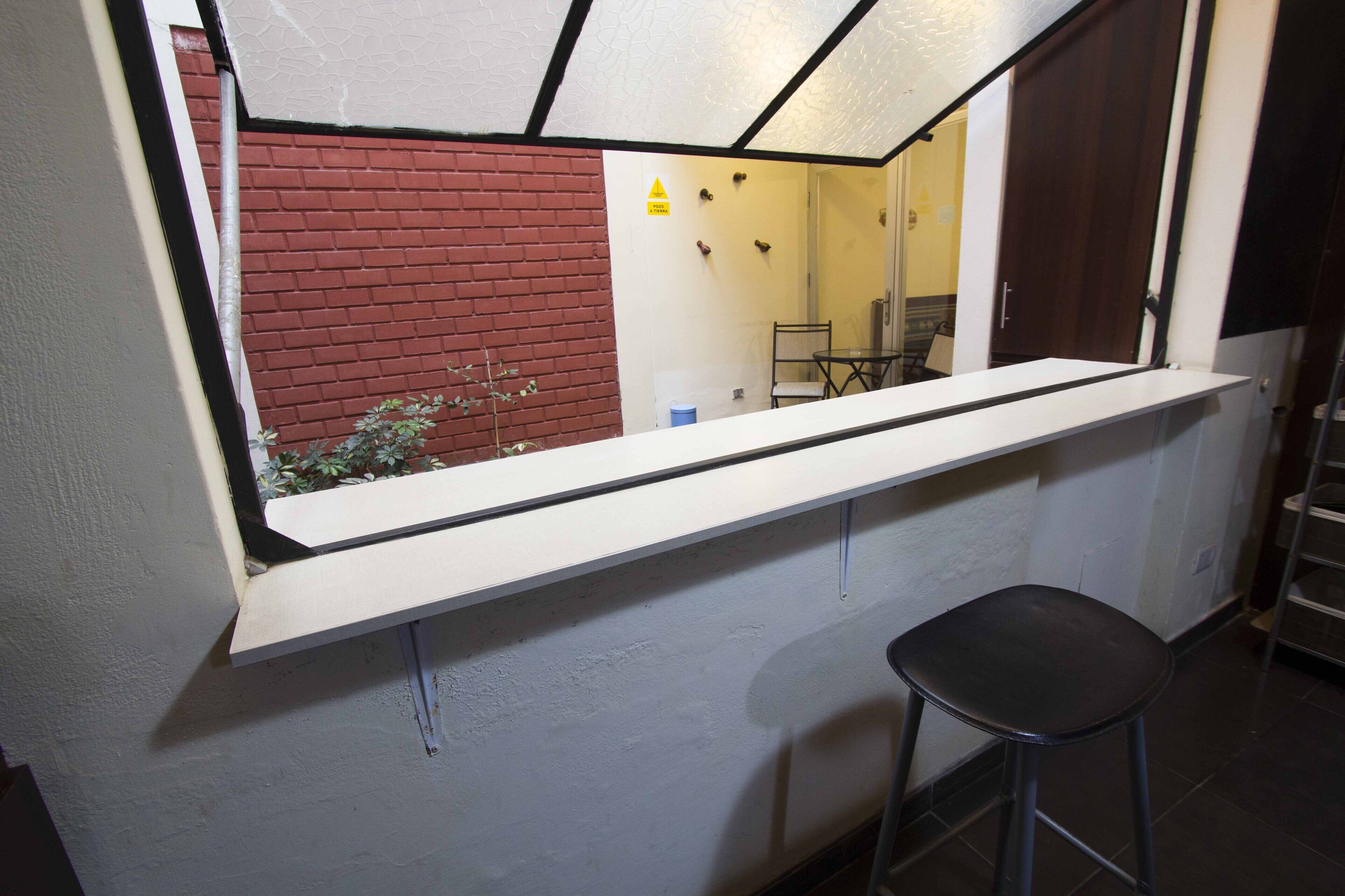 A narrow hallway with a white counter, a black stool, and a red brick wall.