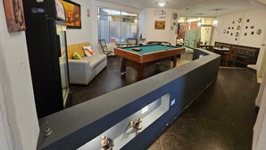 Una mesa de billar en una habitación con un sofá, un refrigerador y un separador de vidrio.