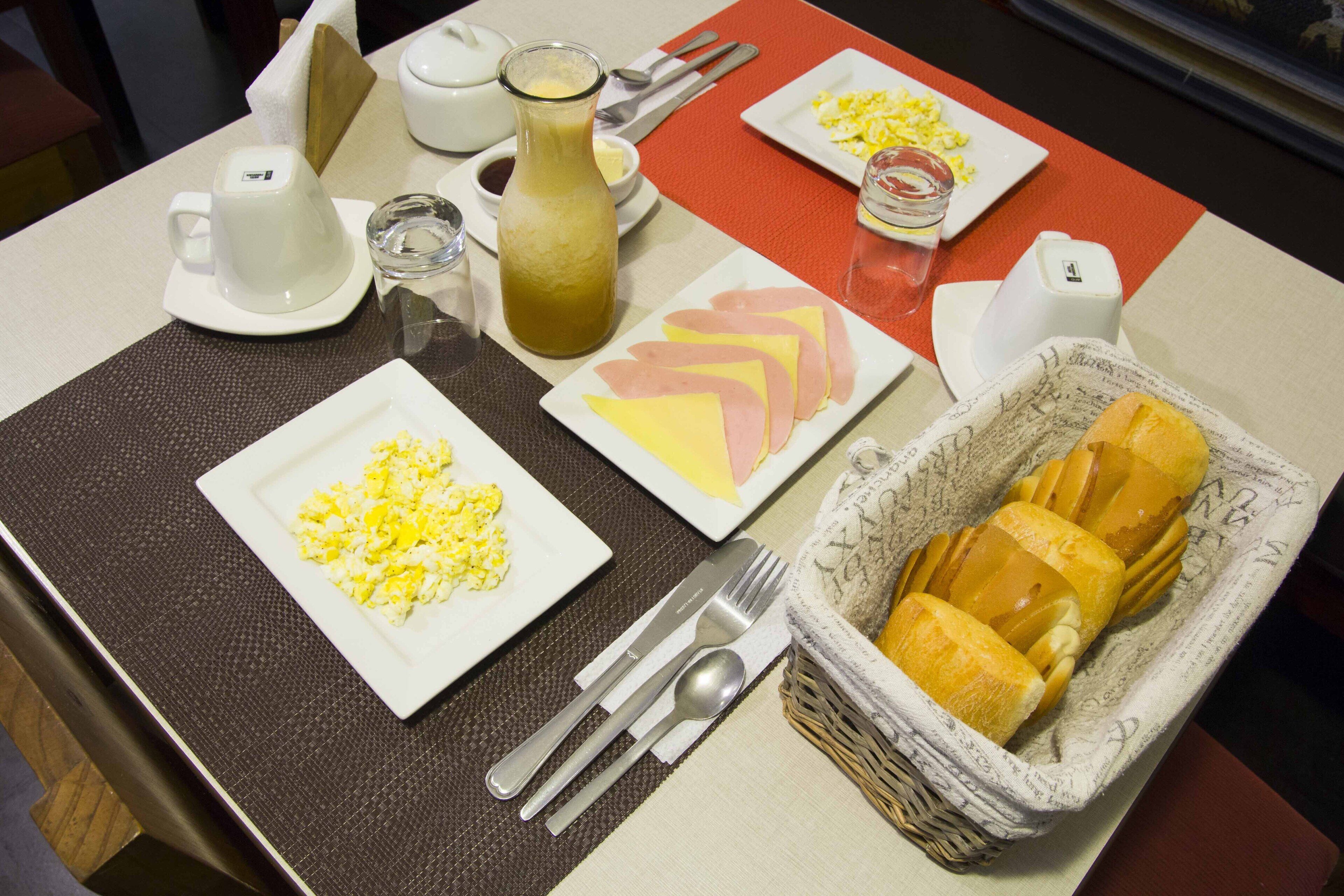 A breakfast setting with plates of scrambled eggs, ham, and toast, along with a glass of juice and a bottle of juice.