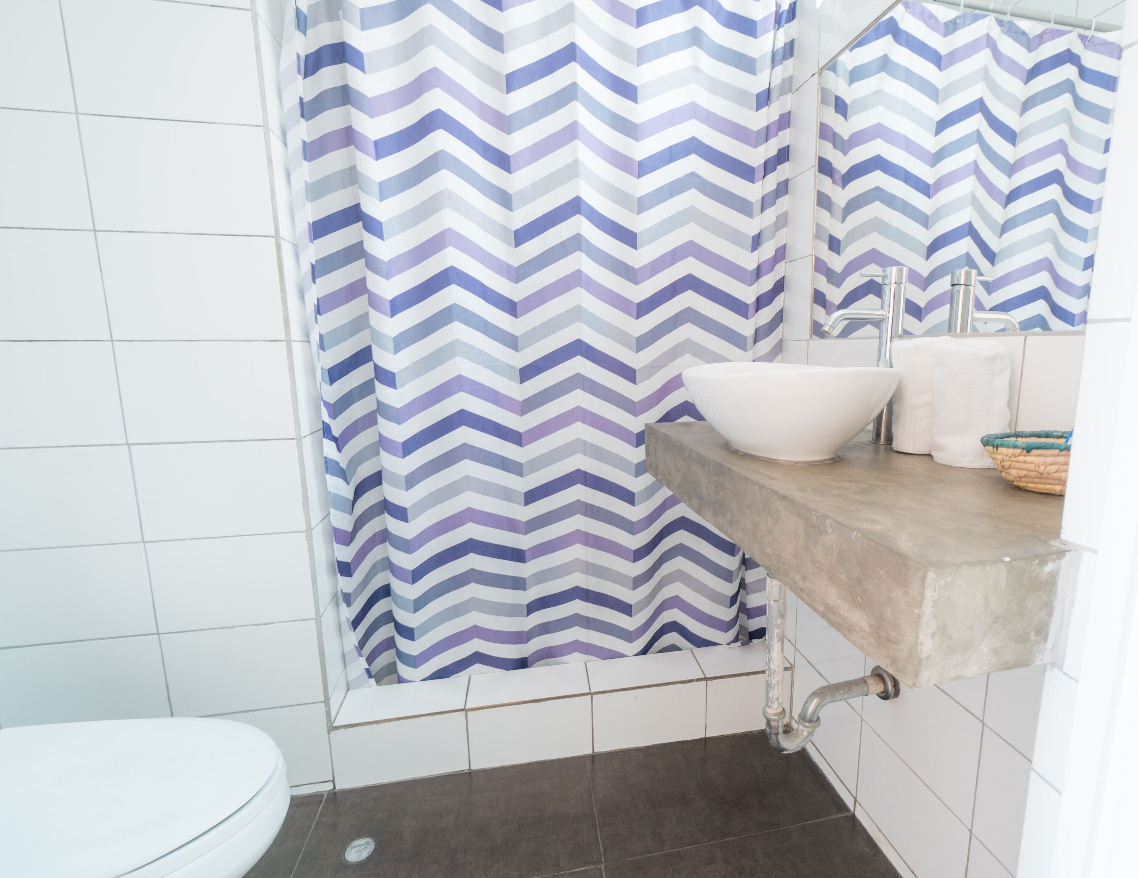 A bathroom with a white toilet, a sink with a white basin, a mirror above the sink, and a shower with a chevron-patterned curtain.