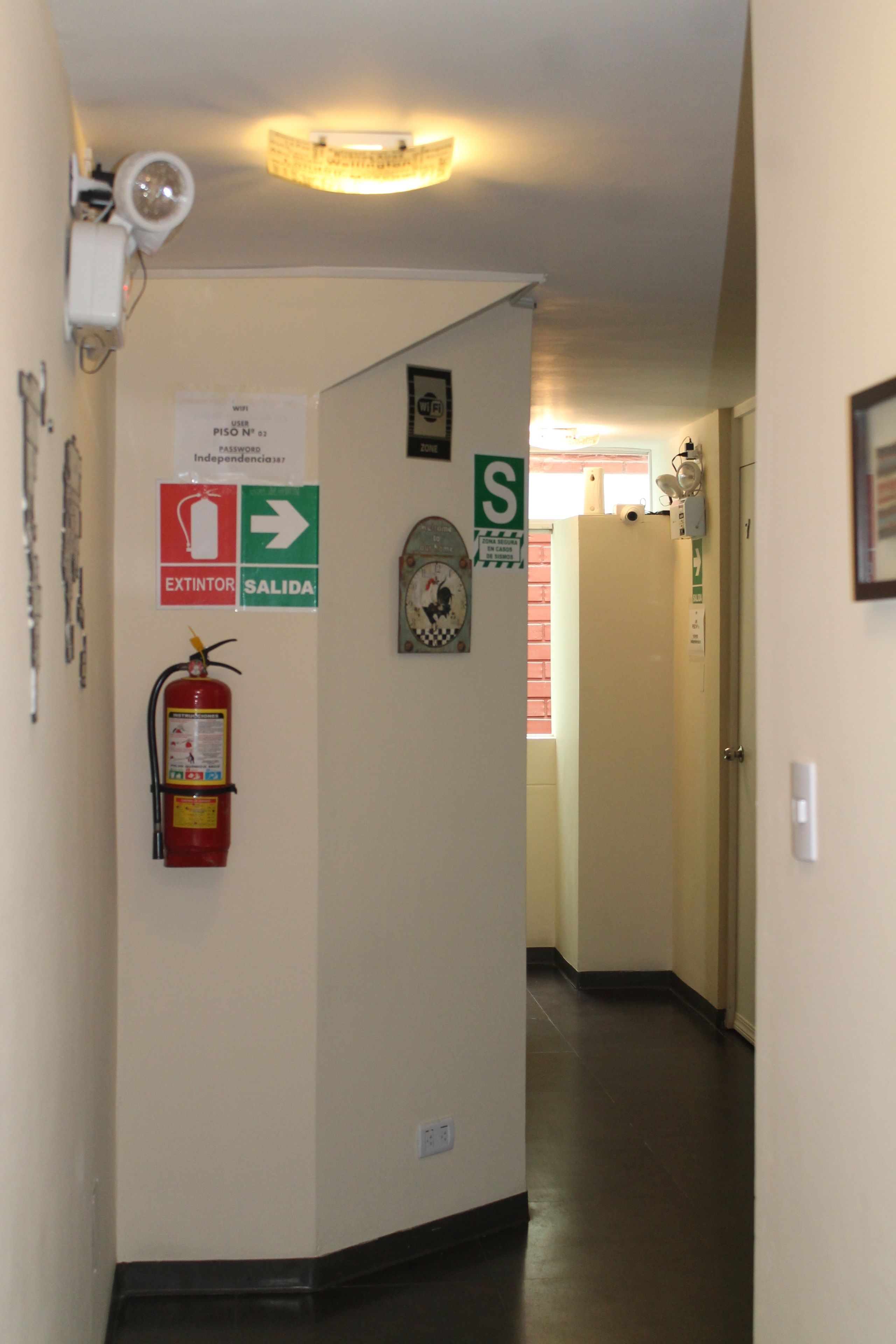 Un pasillo con extintor, letreros de salida y cámara de seguridad.