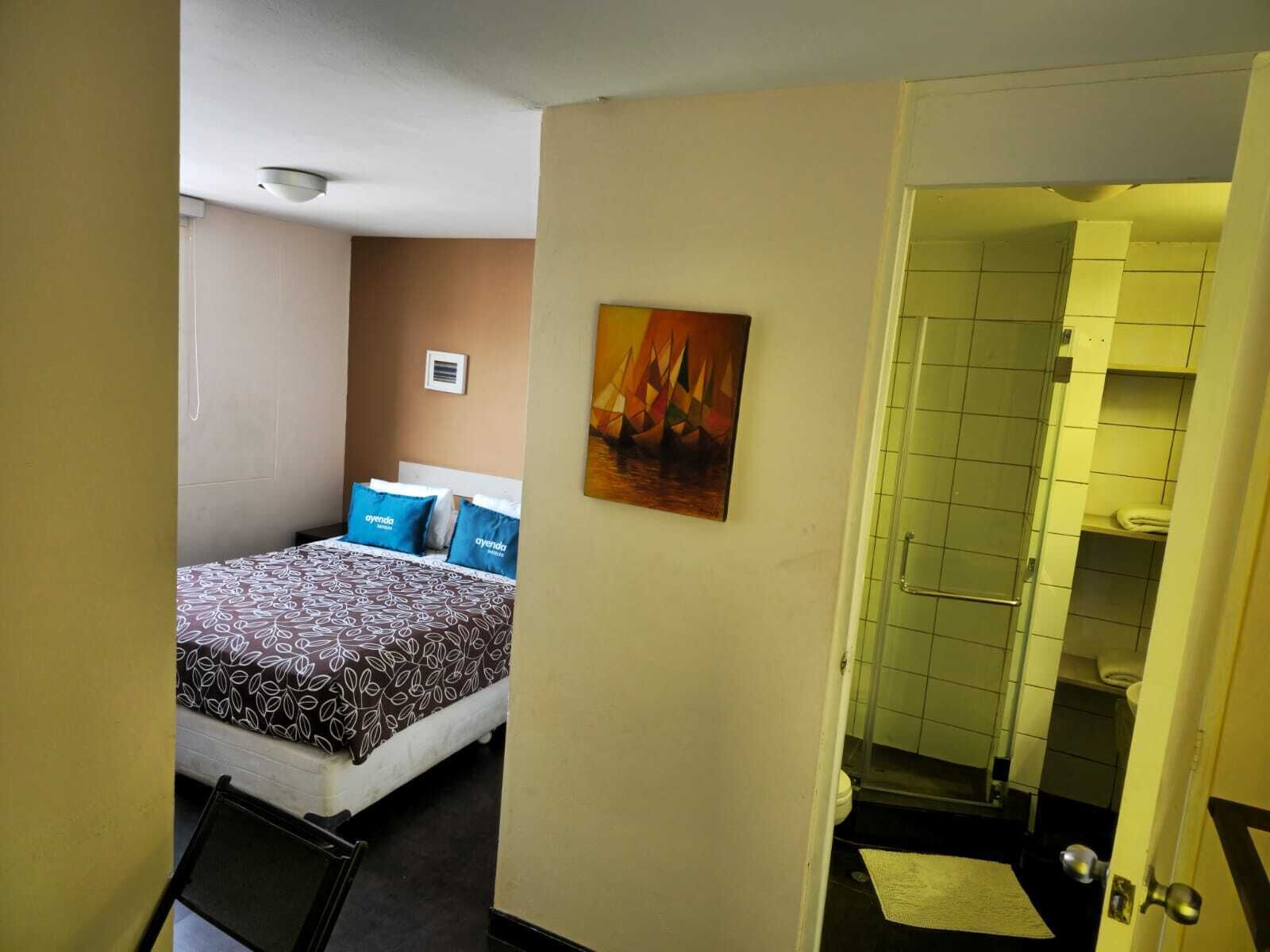 A hotel room with a bed, a painting, and a bathroom visible through an open door.