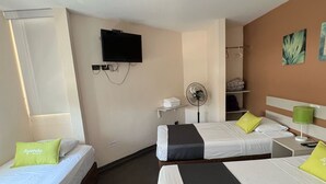 Habitación de hotel con tres camas, televisor, ventilador y ventana.