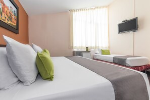 Quarto de hotel com cama, escrivaninha, televisão e janela com cortinas.