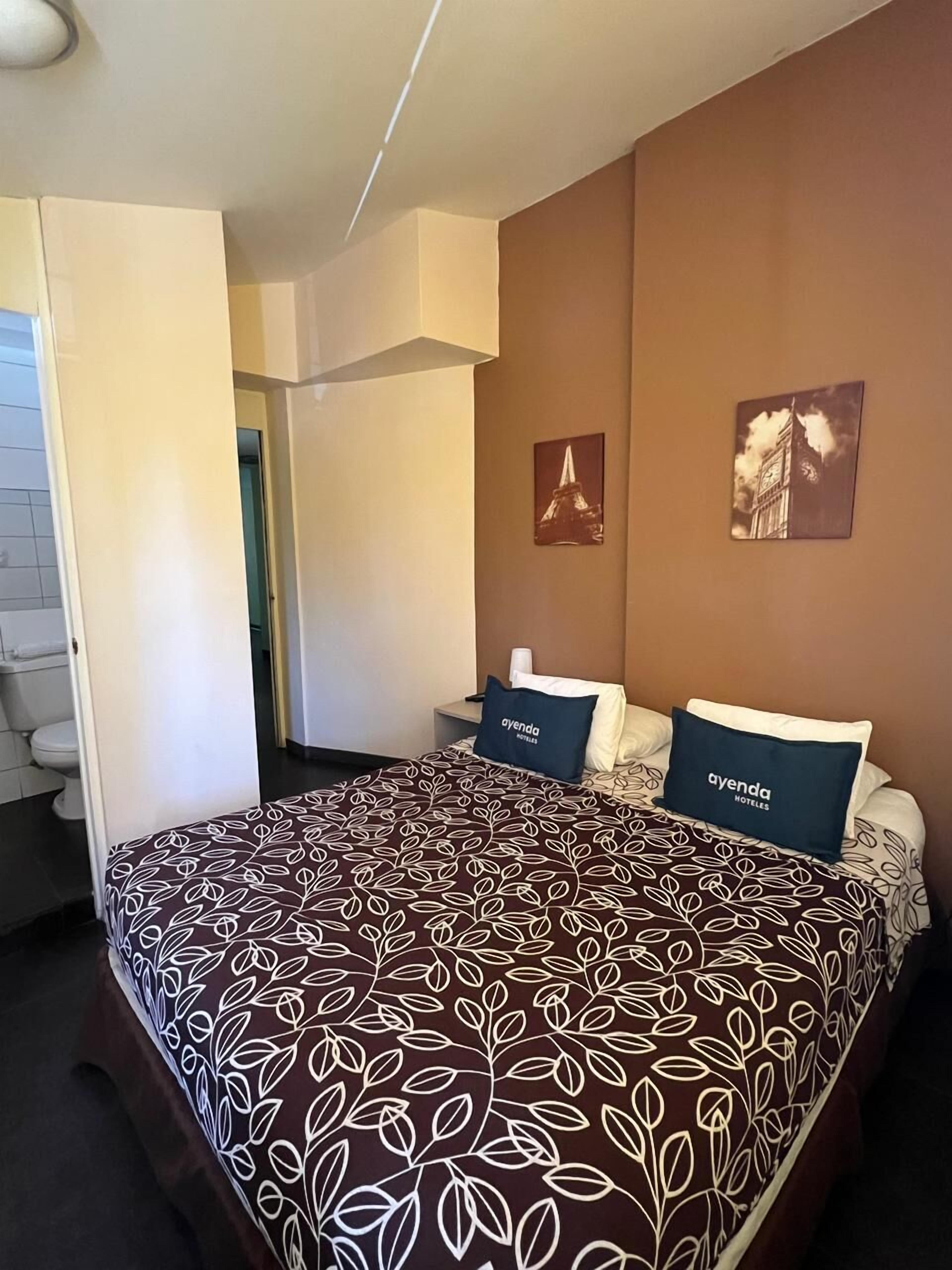 A hotel room with a bed, two pillows with the hotel name, a picture of a tower, and a picture of a clock tower.