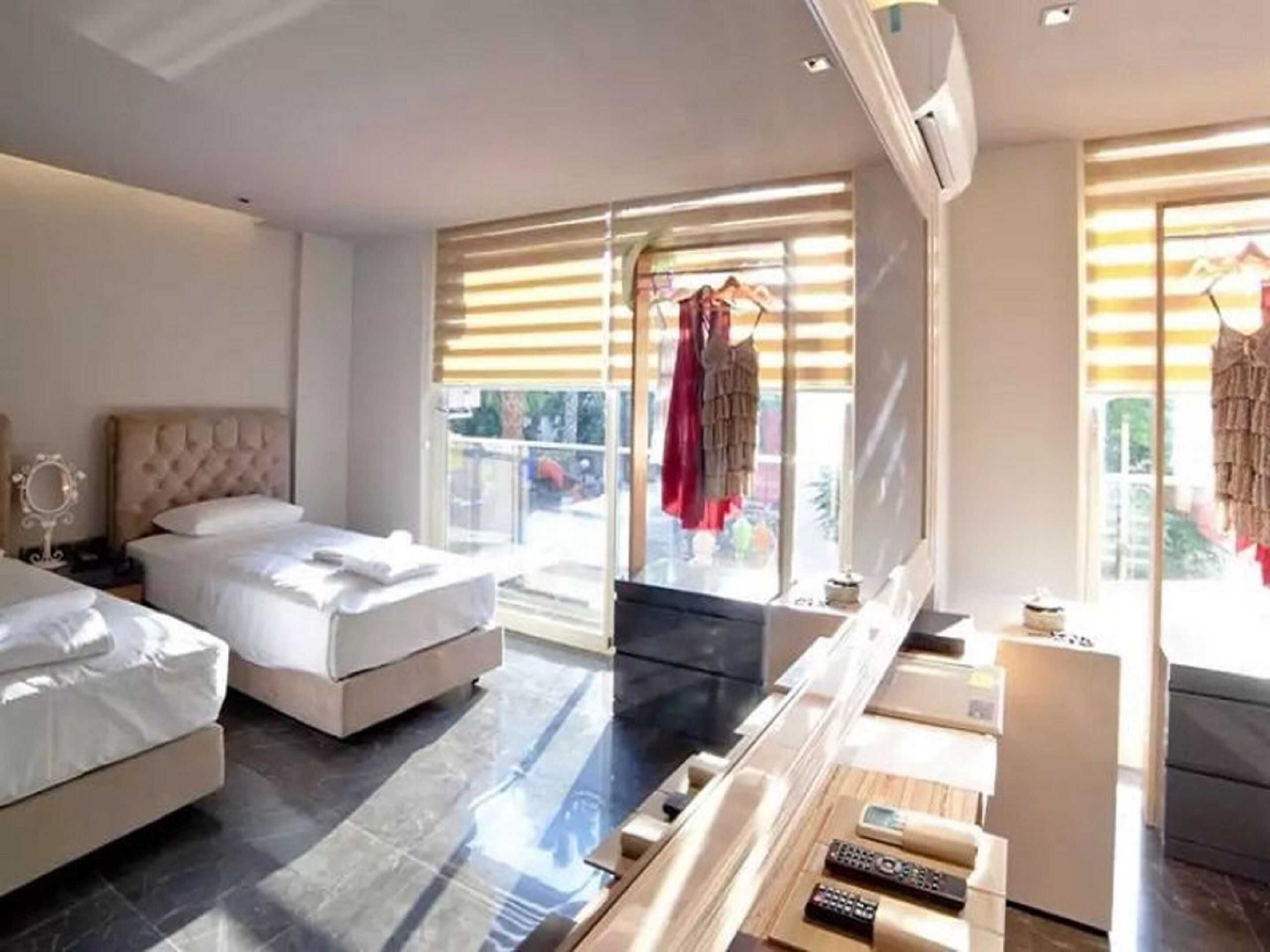 Une chambre d’hôtel moderne avec deux lits, une grande fenêtre avec stores, un téléviseur à écran plat et une petite kitchenette.