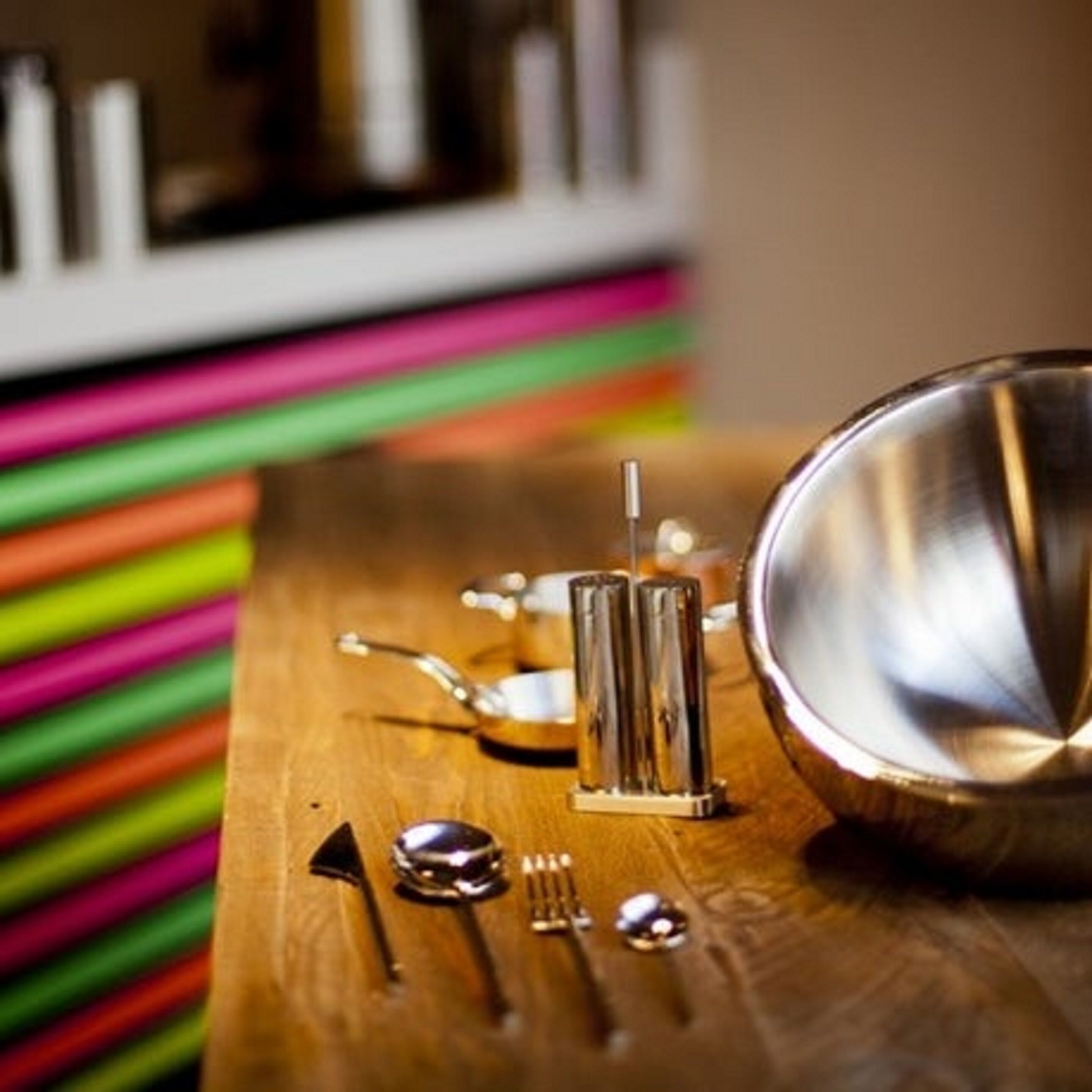 A wooden table with a metal bowl, a glass container, and a spoon.