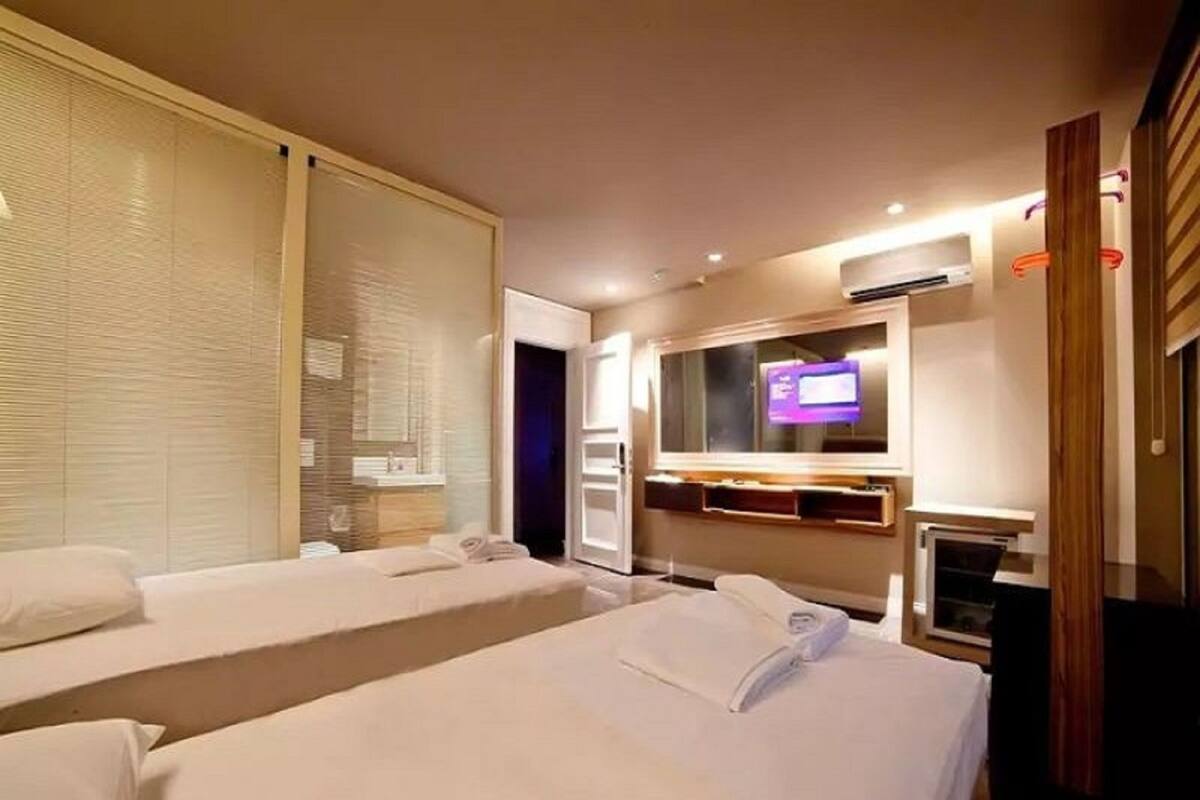 A hotel room with two beds, a television, a mirror, and a window with blinds.