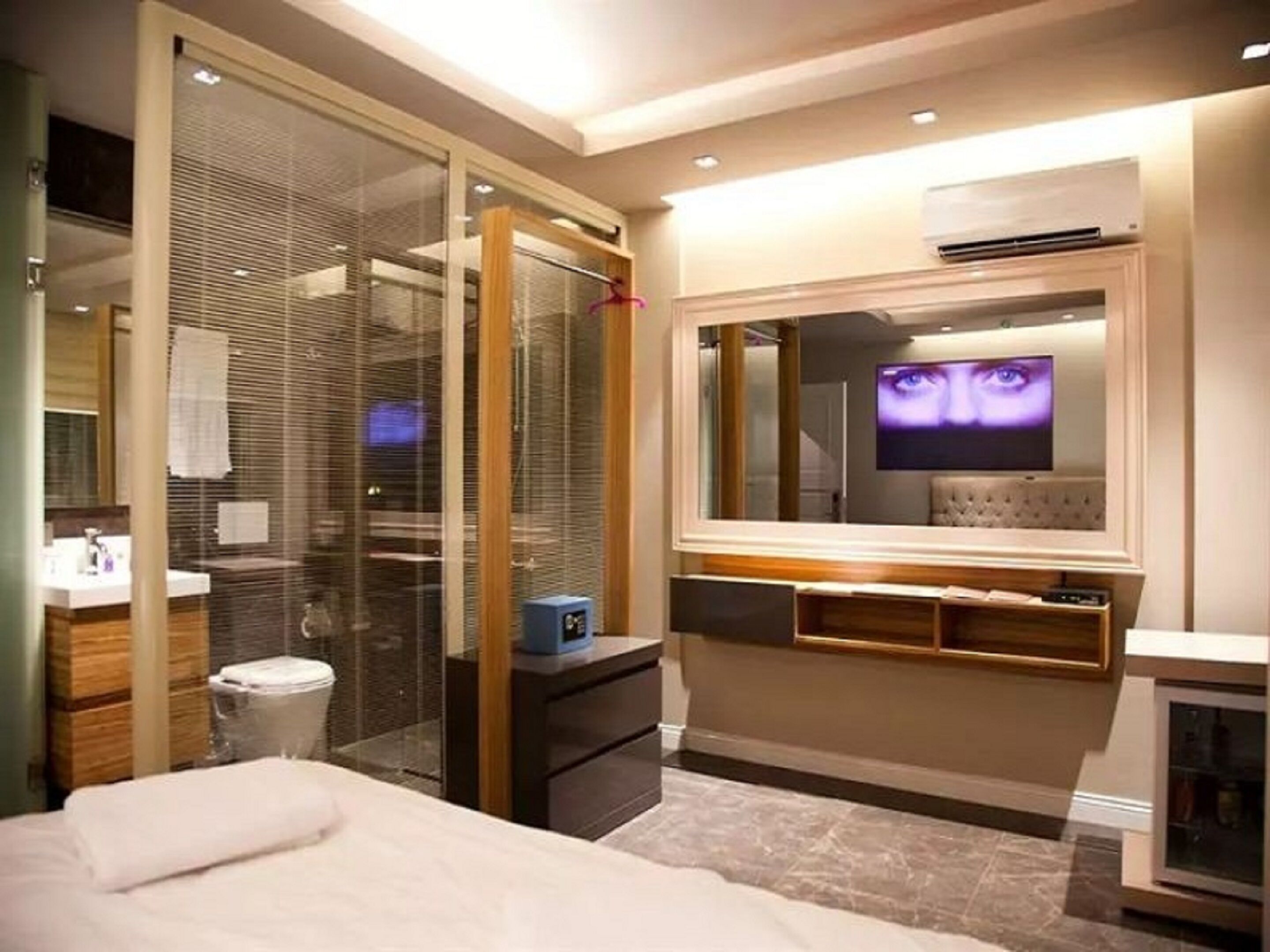 A modern bedroom with a bed, a TV mounted on the wall, and a glass partition.