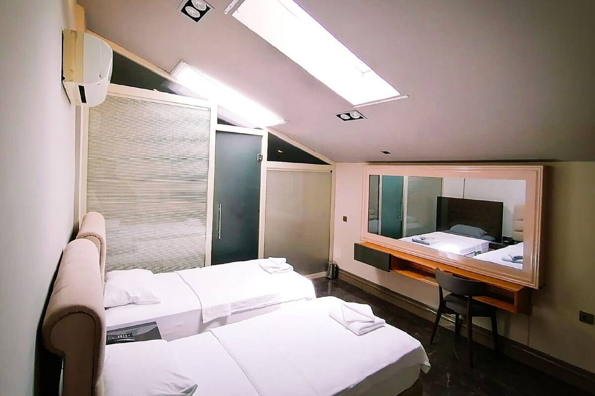 A hotel room with two beds, a desk, a mirror, and a window.
