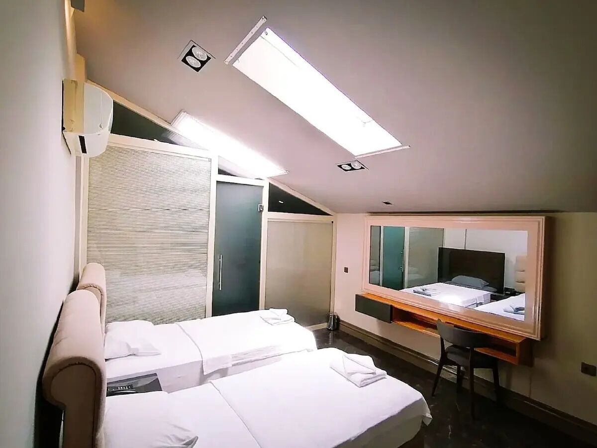 A hotel room with two beds, a desk, a mirror, and a ceiling light.